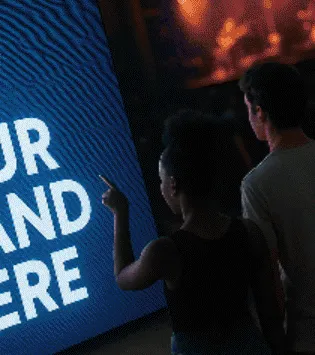 Dos personas señalan una pantalla grande con letras blancas sobre fondo azul