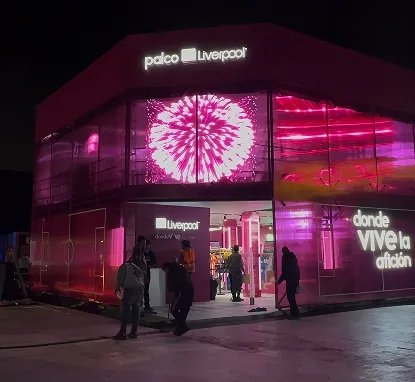 Pabellón de noche con fachada de vidrio iluminada en rosa que muestra fuegos artificiales